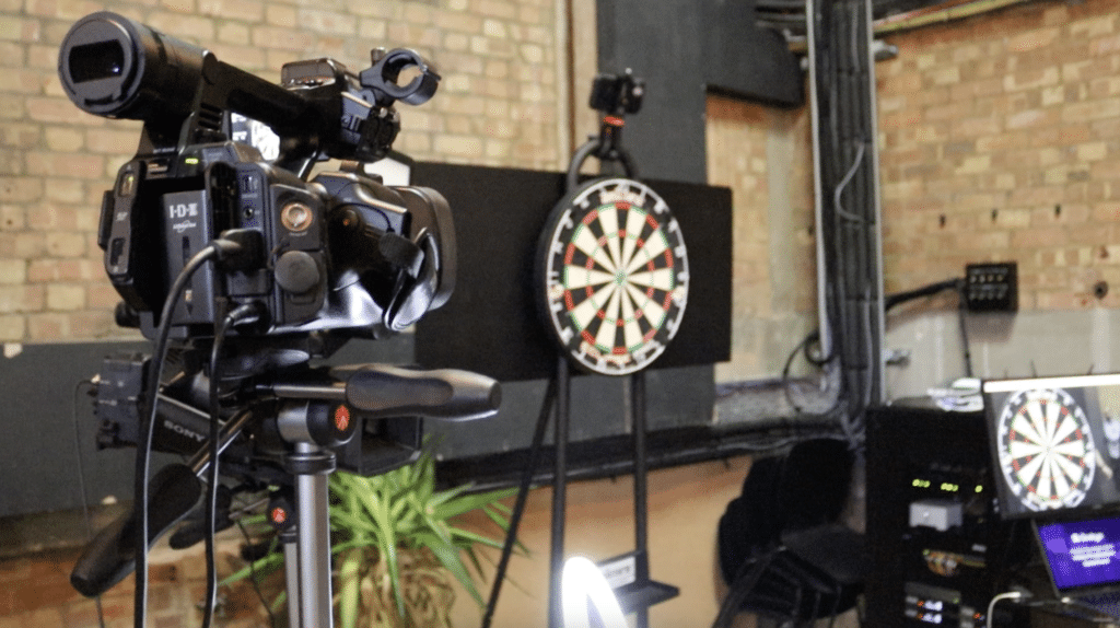 An image of a professional video camera pointing at a dartboard